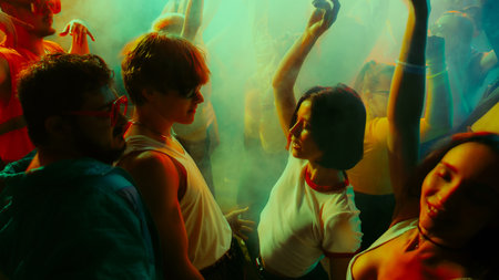 Group of young adults dancing at a vibrant, colorful party with dynamic lighting and fog effects.