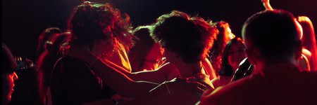 Banner. A dimly lit dance floor scene with people embracing and dancing, illuminated by red and...