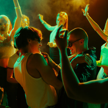 Group of people dancing energetically at a party with colorful lighting.