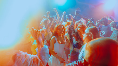 Vibrant party scene with people dancing under colorful lights.の写真素材