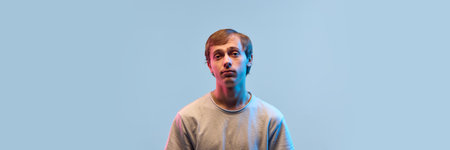 Guy with blank face looking straight in neon light against gradient background feeling tired or lost in thoughts showing low energy and confusion. Bannerの写真素材