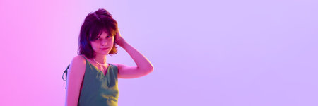 Playful girl in green dress smiling and touching hair under vibrant pink and violet light against gradient background. Bannerの写真素材