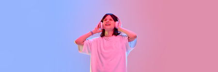 Cheerful girl listening to music with headphones looking up under colorful lights enjoying rhythm...