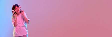Teen girl dancing with closed eyes smiling confidently in oversized clothes under colorful glowing studio light with negative space to insert text. Bannerの写真素材