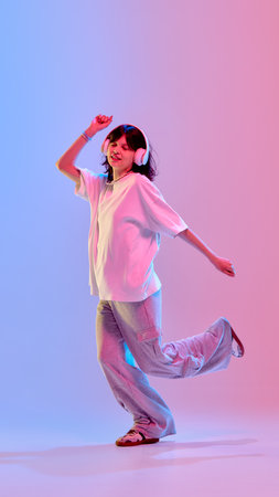 Full length photo of young attractive teen girl dancing of joy and happiness in neon light against gradient studio backgroundの写真素材