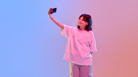 Teen girl posing with phone for selfie smiling confidently in neon light showing attitude and style...