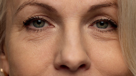 Close-up of mature womans eyes with soft makeup showing natural wrinkles and smooth skin against dark mode backgroundの写真素材