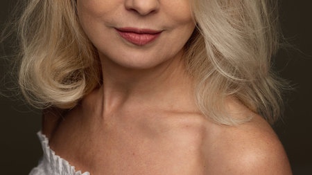 Close-up on cheek and collarbone of mature woman in white top with radiant smooth skin against black backgroundの写真素材