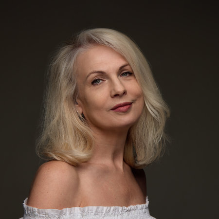 Portrait of confident mature woman with smooth skin and lifted face. with smiling expression against dark studio backgroundの写真素材