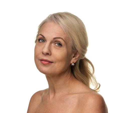 Portrait of elegant woman in 50s, with confident expression and soft makeup, looking straight with grace and relaxed expression against white backdropの写真素材