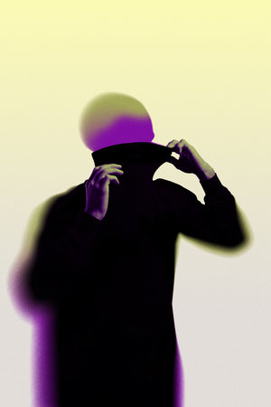 Dark silhouette of figure with hands pulling up high collar, revealing glowing purple and green head, against light yellow background.の写真素材