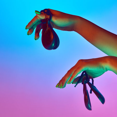 Female hands playing two castanets in mid-air motion under neon lighting against gradient studio...