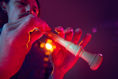 Artistic musician playing plastic recorder with expressive hand positioning under warm stage light against grad9iet purple background.の写真素材