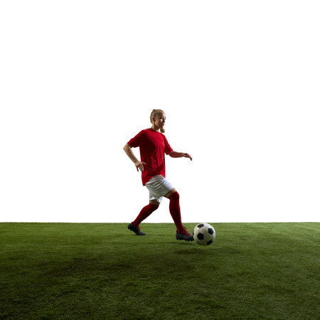 Focused young woman dribbling ball forward during match showing determination on green grassy playground against white backgroundの写真素材