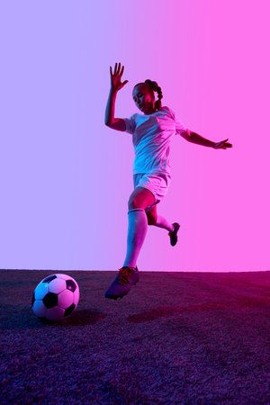 Female athlete sprints with high knee past soccer ball on turf under vibrant purple gradient background. Concept of sportの写真素材