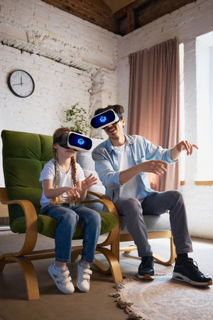 Father and daughter exploring virtual reality with headsets in cozy living room environmentの写真素材