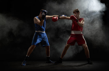 Boxers in blue and red engage in intense fight amidst smoke on dark backgroundの写真素材
