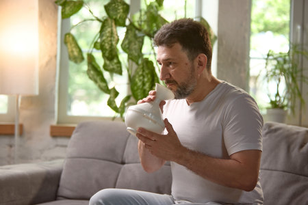 Older man using home inhalation device for respiratory therapy indoors. Men wellnessの写真素材