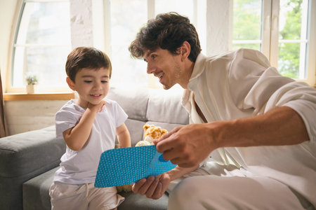 Father and son sharing heartfelt card in bright living room on fathers day celebrationの写真素材