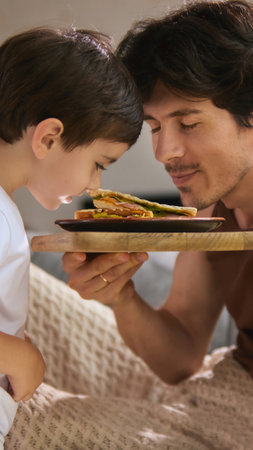 Family moments. Father and son enjoying breakfast in bed with sandwich on Fathers Day morningの写真素材