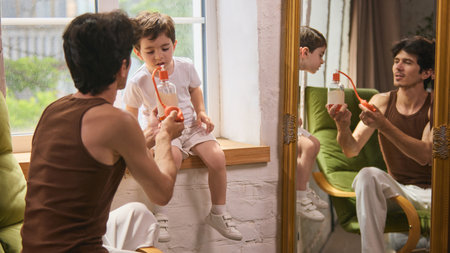 Grooming and identity. Father applying perfume while son watches in the mirrorの写真素材