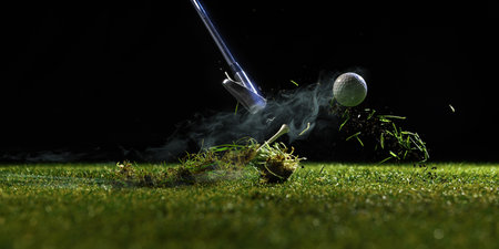 Golf club hitting ball off turf with dirt and grass flying in dark backgroundの写真素材