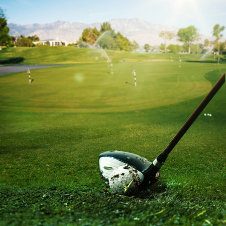 Golf club striking ball on fairway with sprinkler system and distant mountainsの写真素材