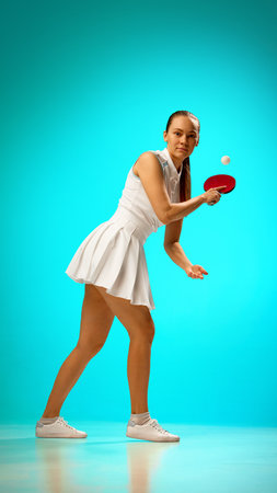 Young woman playing table tennis on vibrant turquoise backgroundの写真素材