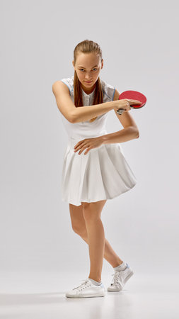 Focused table tennis player in white outfit with red paddle in ready stance full lengthの写真素材