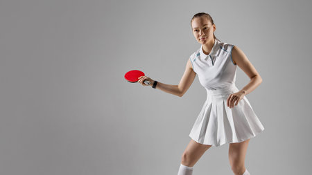 Woman playing table tennis in white outfit on grey backgroundの写真素材