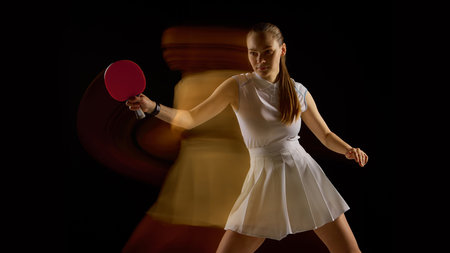 Focused female table tennis player with blurred motion behind on black backgroundの写真素材