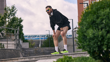 Man in his middle years regaining breath following exercise session in city environment