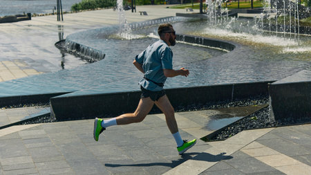 Midlife man jogging beside urban fountains on sunny day