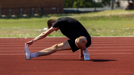Athlete stretches on track in preparation for outdoor sports event during bright daylight
