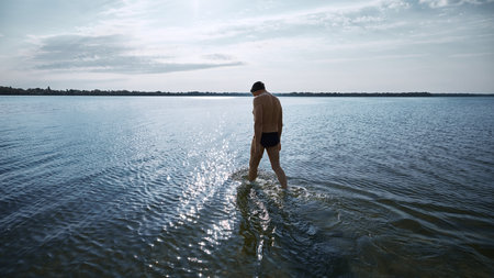 Male swimmer walking into calm lake with contemplative moodの写真素材