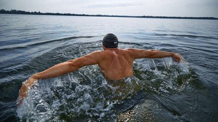 Senior swimmer from behind doing butterfly stroke in open waterの写真素材