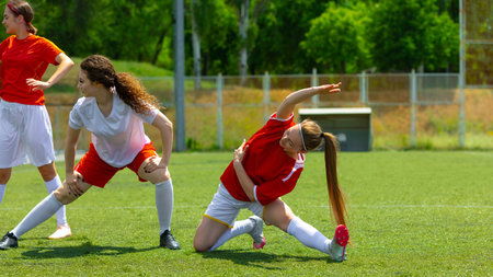 Female football athletes stretching on a sunny day on a grassy fieldの写真素材