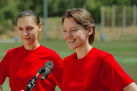 Smiling women football players giving interview on field in red jerseys