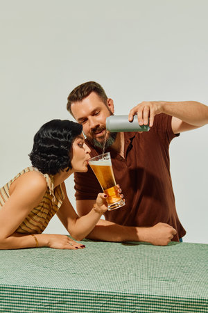 Man pouring beer into large glass as woman drinks directly from it with amused expressionの写真素材