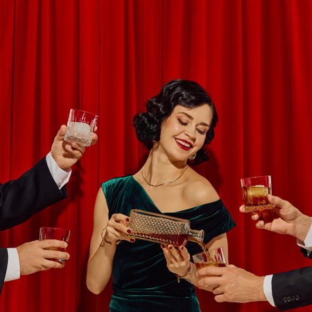 Smiling woman in velvet dress pouring whiskey into glasses surrounded by raised male handsの写真素材