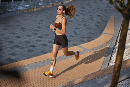 Female running on city walkway with sports attire and sunglasses during morning hours