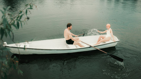 Man and woman laughing and splashing water while rowing boat on river