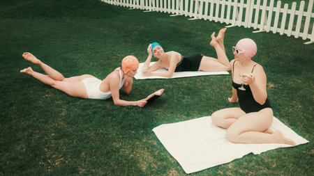 Three women sunbathing on grass in retro swimsuits and swim caps