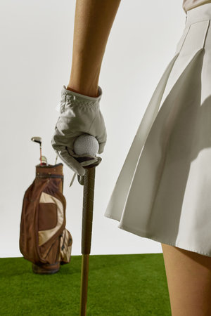 Woman hand in glove holding golf ball on top of club next to bagの写真素材