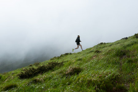 Bright collage of male athlete running uphill on misty green mountain slope