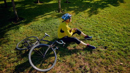 Cyclist resting on grass beside bicycle in shaded park areaの写真素材