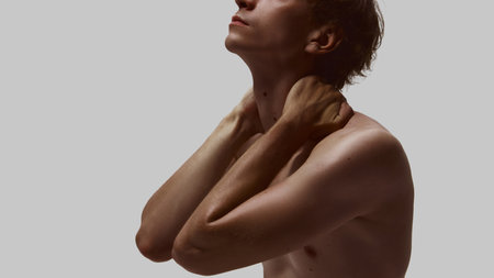 Young shirtless man holding tense neck with both hands, eyes turned upwardの写真素材