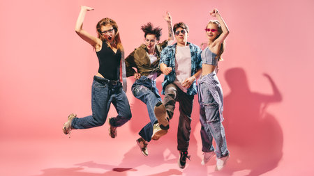 Energetic youth group jumping in stylish streetwear on pink background