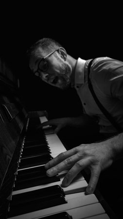 Expressive man in glasses playing piano with wide open mouth in dramatic black and white light
