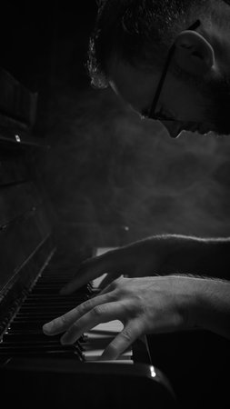 Man focused on piano keys under smoky light with intense concentrationの写真素材